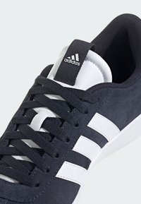 Męskie sneakersy z ciemnoszarego zamszu z białą gumową podeszwą, z białymi paskami i czarnymi sznurówkami. Zawierają czarne logo na pętli pięty.