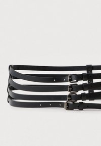 Cinture in pelle nera disposte in fila, dotate di diversi fori per la regolazione e fibbie in metallo argentato con anelli.