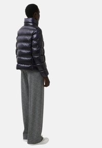 Granatowa kurtka puchowa z wysokim kołnierzem, z pikowanym wzorem, zestawiona z szerokimi, teksturowanymi szarymi spodniami i białymi sneakersami.