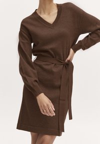 Vestito marrone lavorato a maglia con scollo a V, maniche lunghe e cintura in vita annodata. Presenta polsini a coste e orlo dritto.