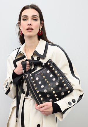 Bolso de mano de cuero negro con tachuelas metálicas plateadas y cristales, cierre con cremallera, asas dobles, con un acabado liso y texturizado.