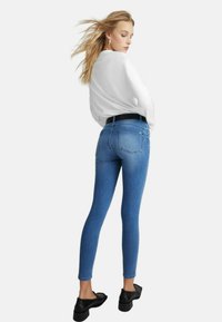 Jeans skinny in denim in un lavaggio chiaro, con un design standard delle tasche posteriori. Abbinati a un top bianco e scarpe nere con tacco a blocco.