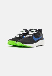 Nike sneakers met een zwarte bovenkant, blauw logo, witte veters en een gestructureerde witte zool, met opvallende groene details op de buitenzool.