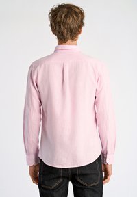 Roze overhemd met lange mouwen van een textuurstof, klassieke kraag en met knoopsluiting, gecombineerd met donkere jeans met contrasterende stiksels.