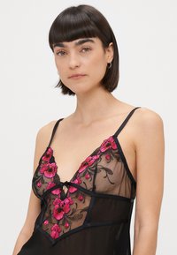 Rochie de noapte transparentă neagră, cu broderie florală în roz vibrant, bretele ajustabile și un detaliu delicat sub formă de fundiță la gât.