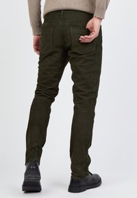 Oliivivihreät housut, jotka on valmistettu pehmeästä, teksturoidusta materiaalista ja joissa on kapea malli. Housuissa on kaksi takataskua ja vähäiset ompeluyksityiskohdat.