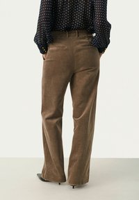 Ruskohva levelegged-pantalonit, joissa on pystyribbaus, korkea vyötärö ja takataskut, yhdistettynä läpikuultavaan tummansiniin pilkulliseen paitaan.