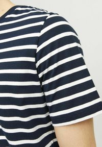 Camiseta de manga corta a rayas en navy y blanco, fabricada en algodón. Presenta un cuello redondo y una textura suave y lisa. Se ajusta estrechamente al cuerpo.