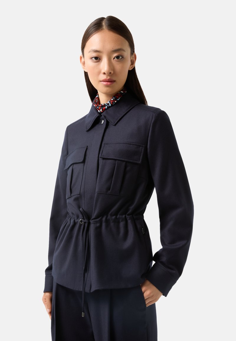 Marineblaue Jacke mit vier Fronttaschen und tailliertem Schnitt; verfügt über einen Kragen und strukturierten Stoff. Akzentuiert mit einem gemusterten Innenkragen.
