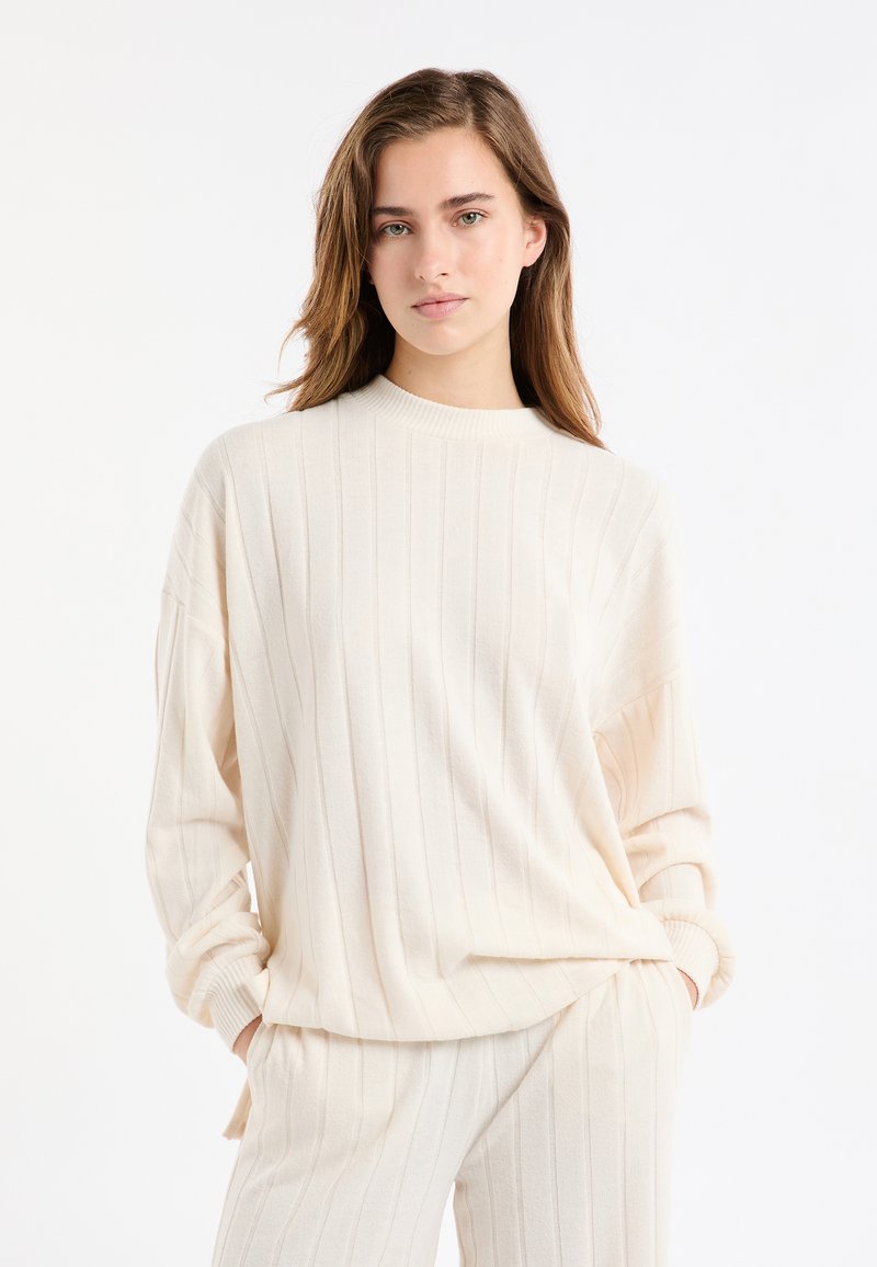 Strickpullover in Cremefarbe mit Rippstruktur, langen Ärmeln und Rundhalsausschnitt, kombiniert mit passenden gerippten Jogginghosen.