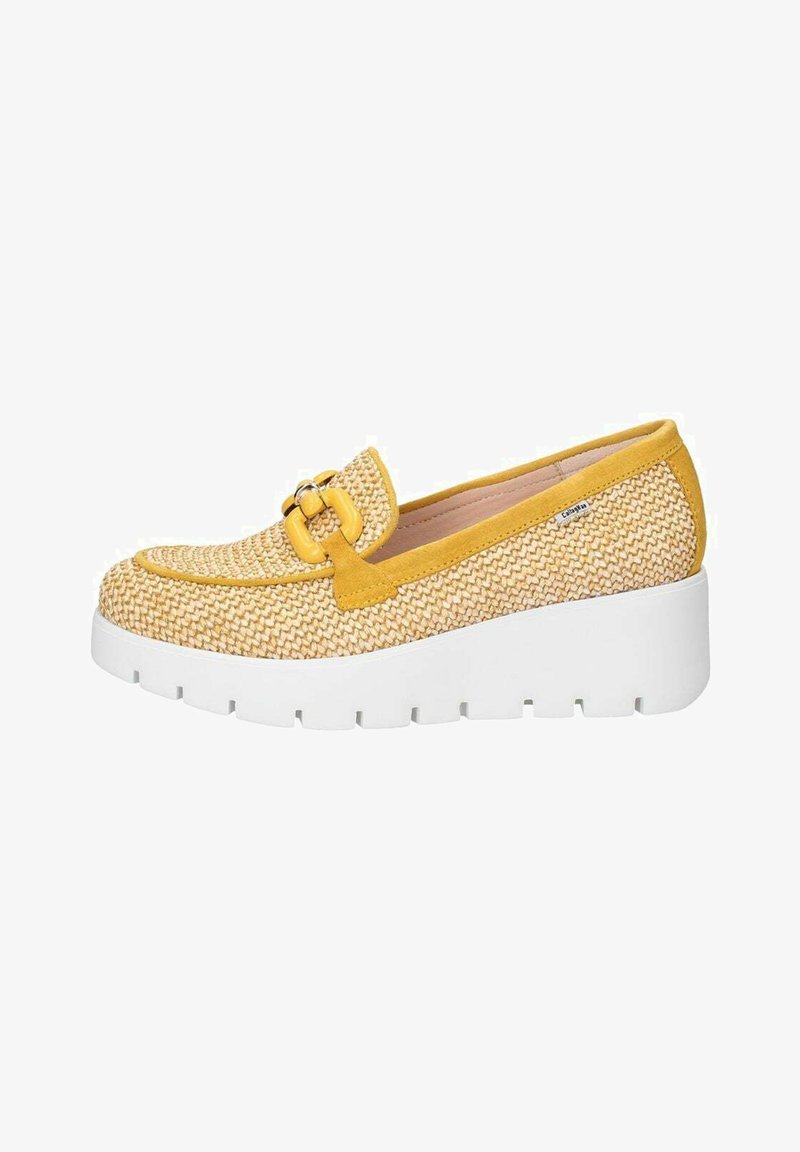 Scarpa slip-on intrecciata gialla e beige con una spessa suola piatta bianca, caratterizzata da una fibbia decorativa sul davanti e una superficie liscia.