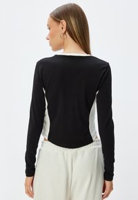 Zwart en crèmekleurig langemouwen shirt met een gebogen zoom en contrasterende zijpanelen, gemaakt van een zachte stof. Heeft een eenvoudige ronde halslijn.