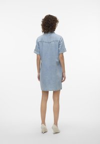 Robe en denim bleu clair avec des manches courtes, un col boutonné et des poignets retroussés. Présente une coupe droite et un détail de empiècement au dos. Texture lisse.
