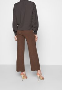 Blouse à manches longues gris foncé et pantalon large côtelé marron. Les chaussures sont couleur nude avec des lanières fines et des talons hauts.