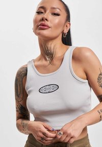 Grijze geribbelde tanktop met een zwart grafisch logo op de borst. Gemaakt van rekbaar materiaal, heeft het een ronde halslijn en brede armsgaten.