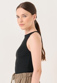 Schwarzes, geripptes Tanktop mit tailliertem Design, runder Ausschnitt und breiten Trägern. Kombiniert mit beigen, Hose mit Kordelzug in der Taille.