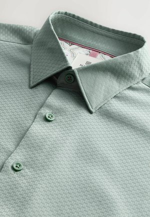 Chemise boutonnée vert clair avec un motif texturé, dotée d'un col écarté et de boutons verts. Motif intérieur visible sur le col.