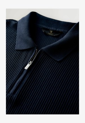 Marinblå ribbad polo med dragkedja framtill, med en slät krage och dragkedja i silver. Mjuk textur och diskret design.