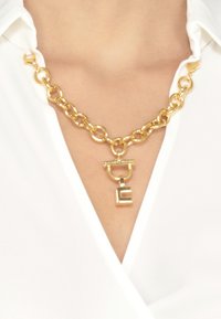 Collana in oro con grandi anelli e un ciondolo rettangolare che presenta una lettera "E" stilizzata e un'accanto circolare.