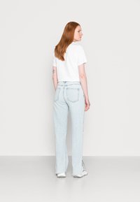 T-shirt cortado branco, jeans de cintura alta azul clara, perna reta, tecido desbotado, vista traseira mostrando detalhes mínimos e costura padrão.