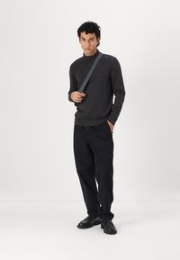 Pulover tricotat de culoare gri închis, cu un design cu jumătate de fermoar, asortat cu pantaloni negri lejeri și pantofi negri, având o curea de umăr gri.