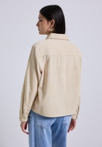 Beige ribfluwelen shirt met een kraag, lange mouwen en knoopmanchetten. Structuurstof met verticale ribbels.