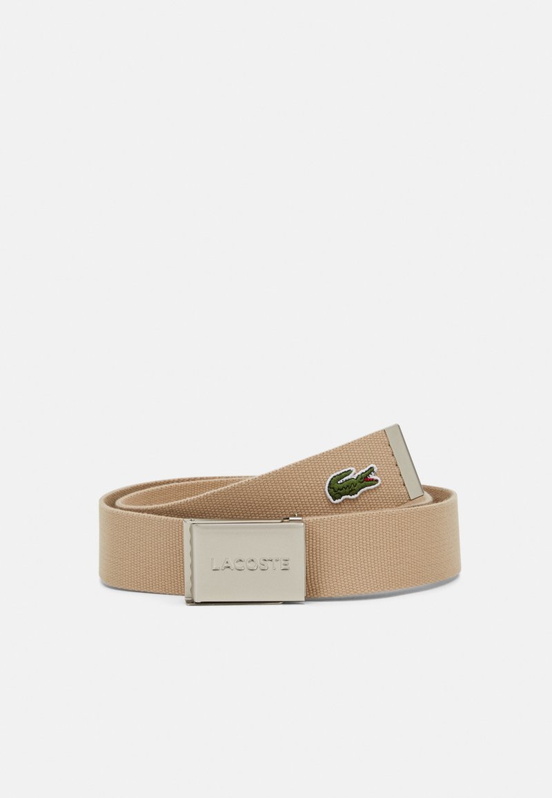 Cinturón de tejido beige con una hebilla de metal plateado que presenta el logo grabado "LACOSTE" y un logo de cocodrilo verde en la correa.