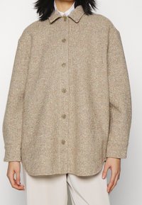 Veste oversize en laine beige avec un tissage texturé, fermeture par boutons et un col, présentant des éclats multicolores dans le tissu.