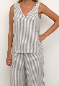 Haut sans manches rayé en blanc et bleu marine, présentant un décolleté en V et une coupe décontractée. Fabriqué en tissu léger avec une texture lisse.