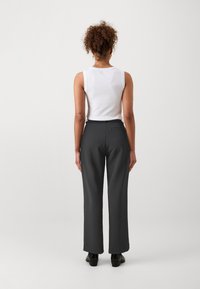 White sleeveless top paired with high-waisted, straight-leg dark gray trousers and black footwear, viewed from the back.