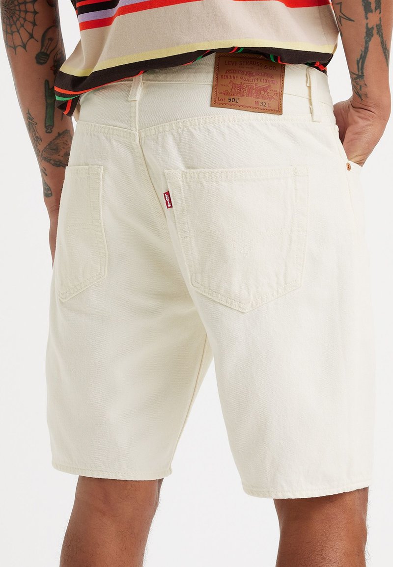Weiße Denim-Shorts mit geradem Schnitt, ausgestattet mit Gesäßtaschen und einem Lederpatch am Bund. Sichtbare Nähte und Etikettendetails.