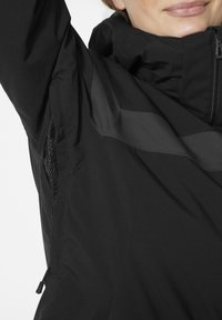 Černá bunda s vysokým límcem, zipem vpředu, síťovinou pod paží a texturovanými panely pro zvýraznění designu.