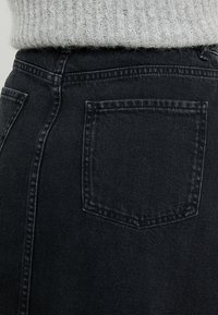 Svarta denimbyxor med en synlig bakficka. Texturen ser hållbar ut. Midjebandet har en lätt avsmalning som kompletterar den övergripande skräddarsydda passformen.