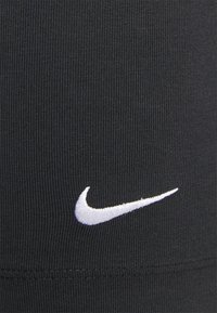Zwarte sportstof met geribde textuur, voorzien van een witte geborduurde Nike swoosh-logo aan de zijkant.