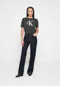 Γκρι κοντομάνικη μπλούζα με λευκό λογότυπο "CK", σε συνδυασμό με σκούρο μπλε ψηλόμεσα τζιν με ίσια μπατζάκια και μαύρα παπούτσια με μυτερή μύτη.