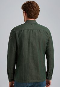 Chemise verte à manches longues en tissu texturé, avec des poignets à boutons, des accents d'épaule et un design de dos avec empiècement. Coupe ajustée.