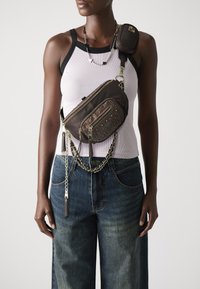Sac en nylon marron à bandoulière avec plusieurs poches zippées et des détails cloutés. Comprend une chaîne en bandoulière et une pochette compacte attachée.