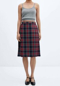 Débardeur gris en tricot, jupe à carreaux bleu marine, rouge et vert, longueur genou avec des boutons sur le côté, et chaussures de ville noires.