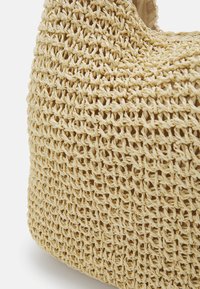 Sac en fibres naturelles tissées de couleur beige, présentant un design complexe à tissage ouvert et une doublure intérieure douce et lisse.