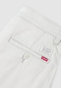 Poche de pantalon Levi's blanche avec fermeture à bouton, étiquette rouge Levi's et label de garantie de qualité Levi Strauss cousu au-dessus de la poche.