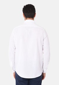 Camicia bianca in lino a maniche lunghe, con colletto a punta e polsini abbottonati, caratterizzata da un orlo dritto e una trama minimale.