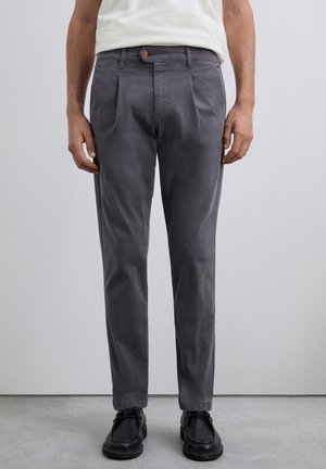 Pantalones de vestir grises con un corte recto, con pliegues en la parte frontal, un cierre de botón y una textura suave, combinados con zapatos negros.
