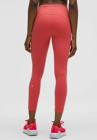 Leggings rosas de cintura alta y ajustados con una textura suave. Presentan una costura trasera y un logo bordado en el tobillo.