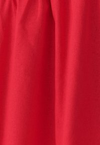 Czerwona tkanina o gładkiej i delikatnie fakturowanej powierzchni, z fałdami tworzącymi wizualną głębię. Brak widocznych wzorów czy elementów metalowych.