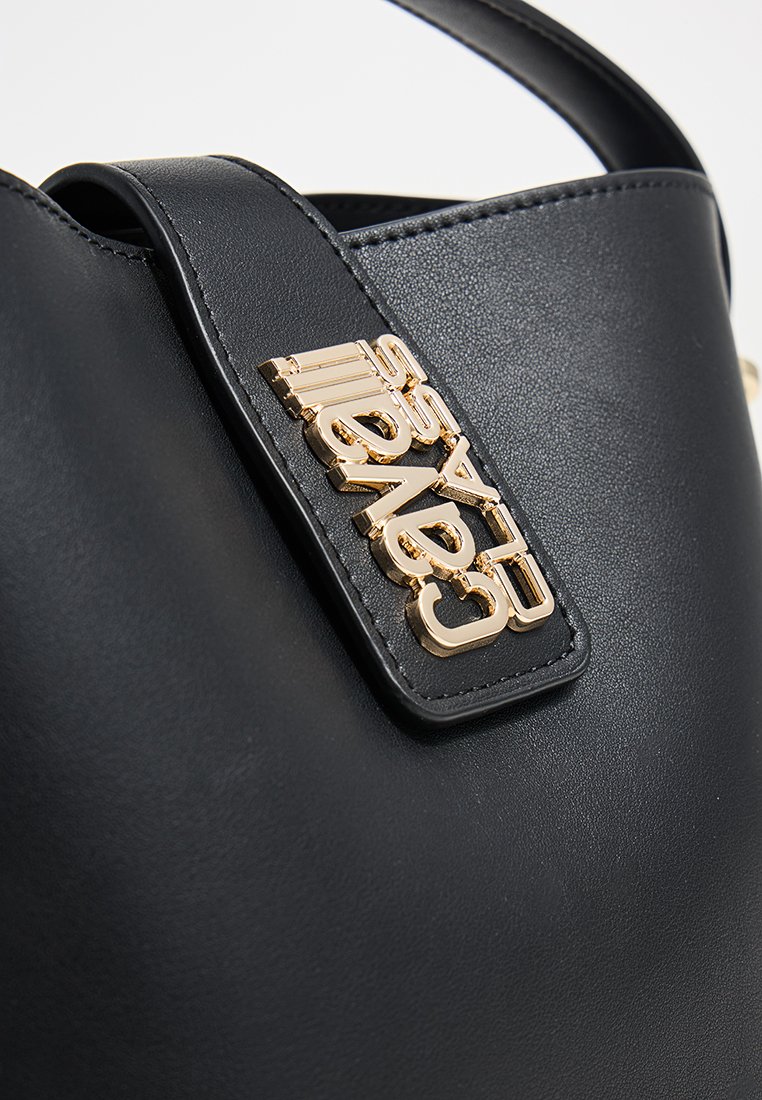 Sac en cuir noir avec un logo en métal doré portant l'inscription "Sergio Cavelty" sur la sangle près de la poignée.