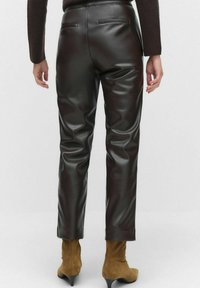 Bruine faux leren broek met een stijlvolle uitstraling, voorzien van achterzakken en een getailleerde pasvorm, gecombineerd met tankleurige high-heeled laarzen.