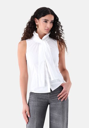 White sleeveless blouse with a tied neck scarf, featuring a smooth texture and slim fit, paired with grey high-waisted jeans.