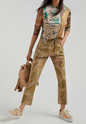 Haut à manches longues à motifs floraux dans des tons terreux ; pantalon beige clair avec imprimés de feuilles de palmier verts ; baskets beiges ; sac minimaliste.