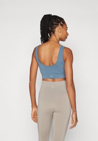 Blå crop top laget av myk stoff med rund hals og brede stropper, kombinert med beige høytlivs leggings. Minimal logo detalj.
