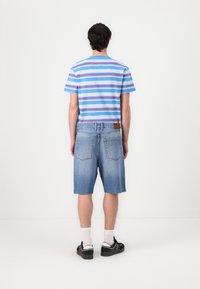 Stripet blå T-skjorte og falmede denimshorts. T-skjorten har horisontale røde og blå striper. Shortsene er knelengde med slitte kanter.